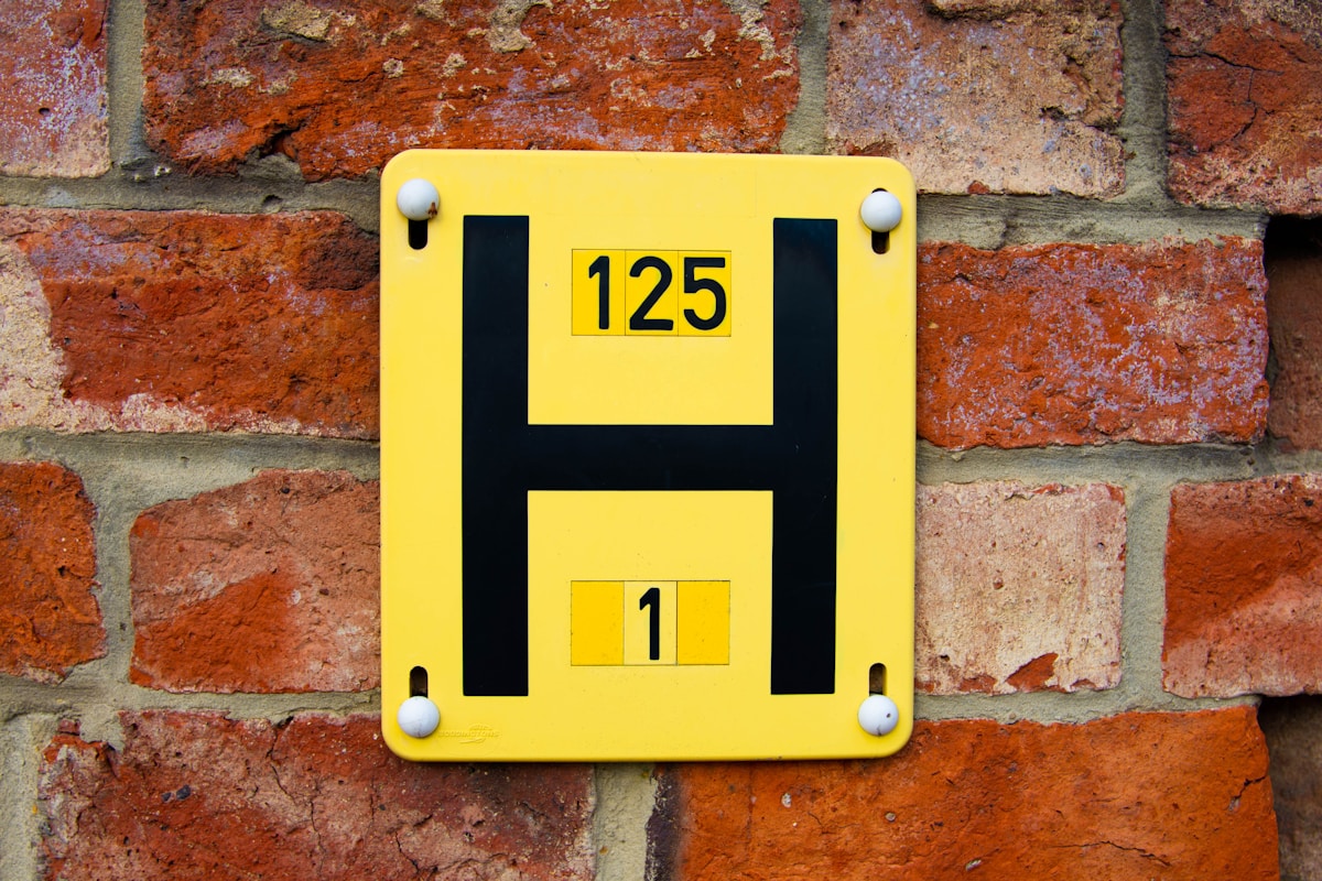 Plaque jaune numérotée sur un mur de briques rouges.