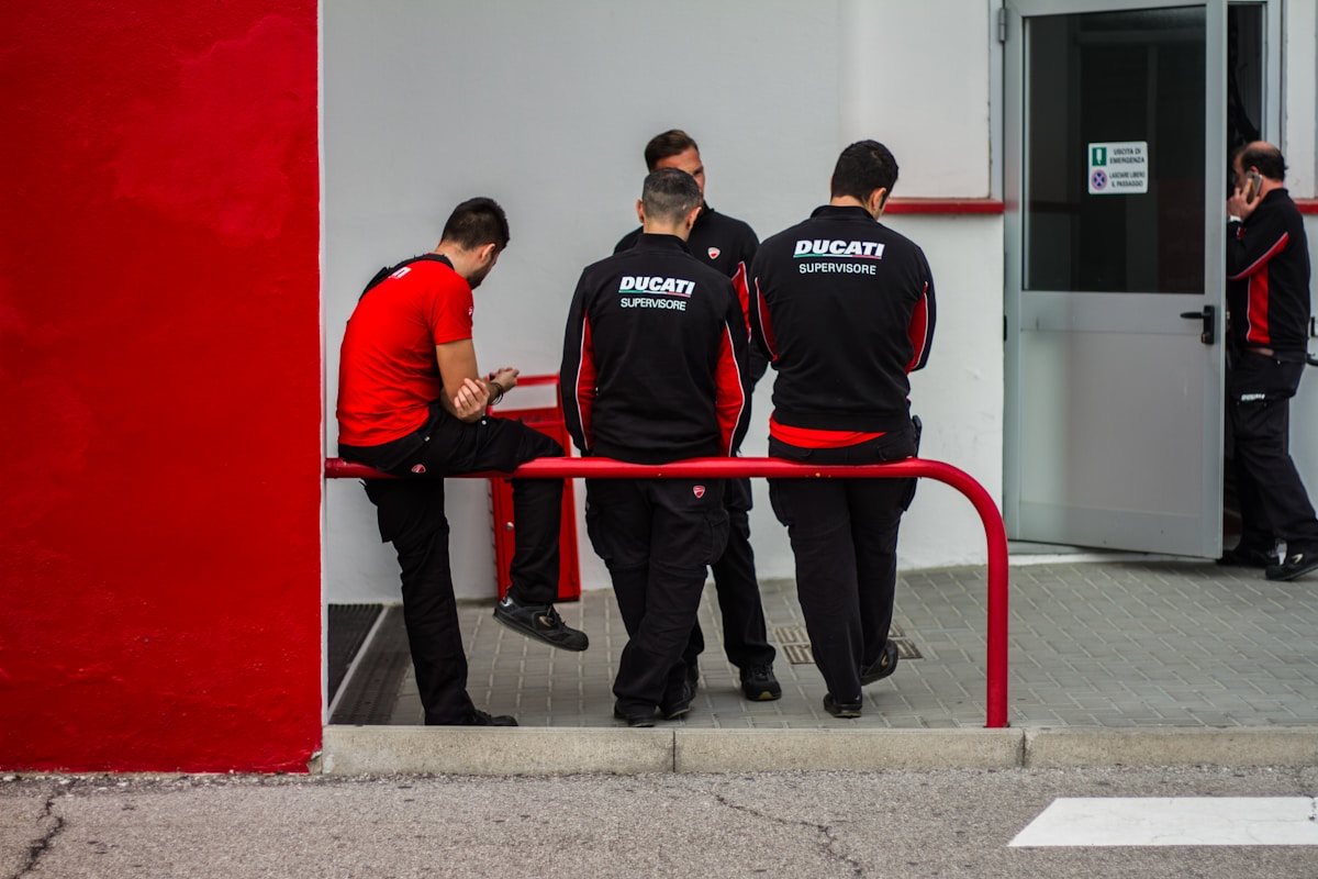 Trois hommes en chemises manches longues noires et rouges debout devant un mur rouge.