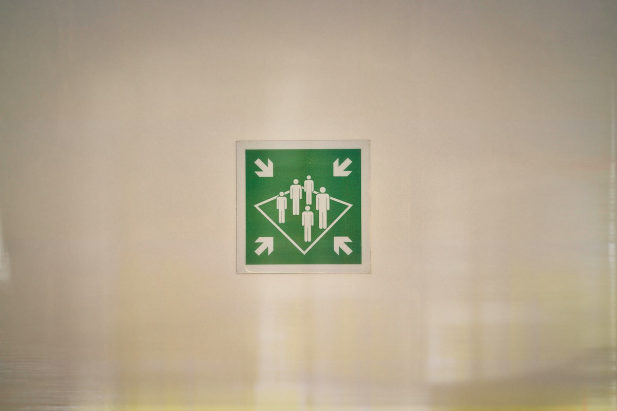 Panneau vert avec pictogrammes de personnes et flèches indiquant le point de rassemblement