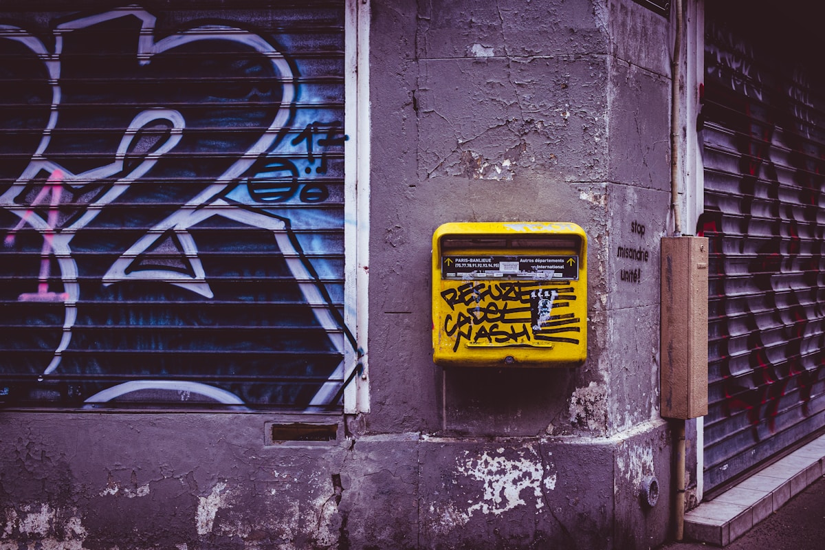 Graffiti mural, boîte aux lettres jaune, mur délavé, ombre et lumière, ambiance urbaine.