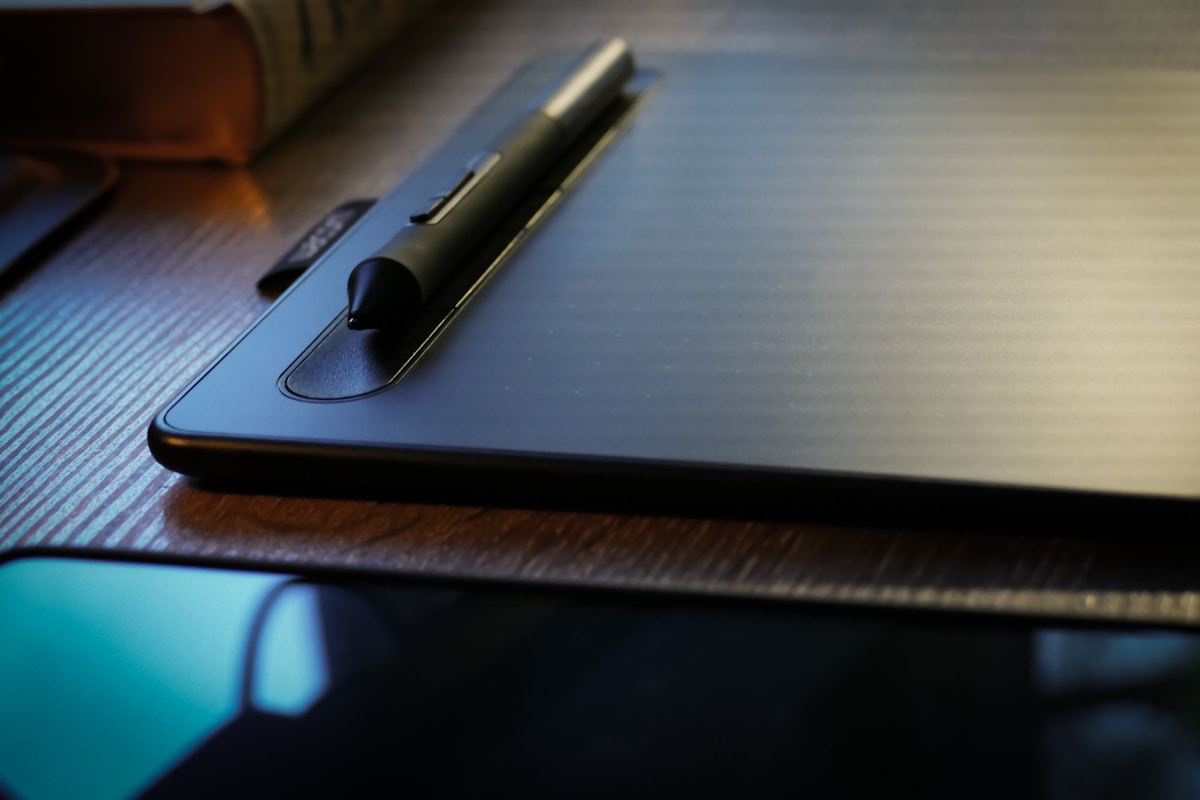 Tablette graphique noire avec stylet sur un bureau en bois.