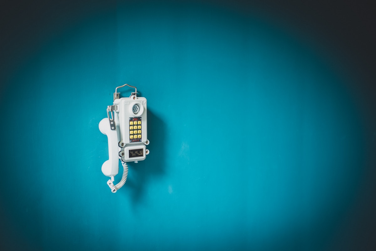 Téléphone public vintage blanc sur fond bleu turquoise.