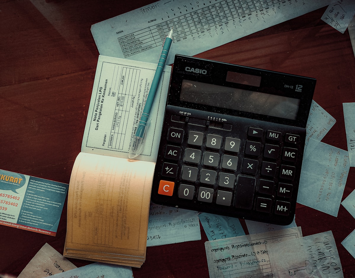 Calculatrice Casio, factures, notes manuscrites, stylo sur une surface sombre.