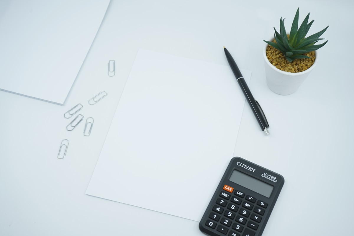 Une calculatrice noire à côté d'un stylo noir sur du papier d'imprimante blanc.