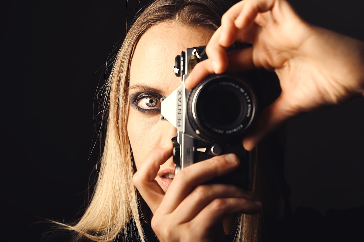 Femme tenant un appareil photo devant son visage.