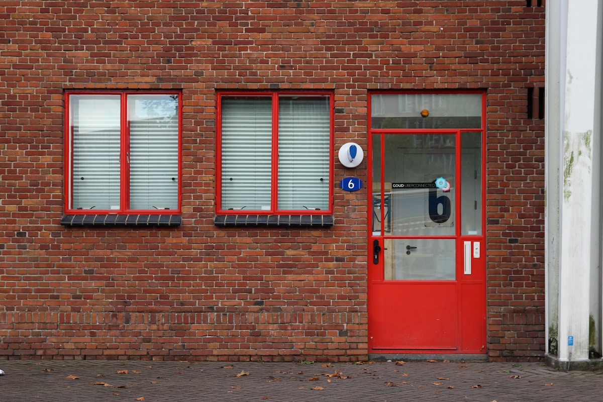 Façade de bâtiment en briques rouges avec fenêtres et porte d'entrée rouges.
