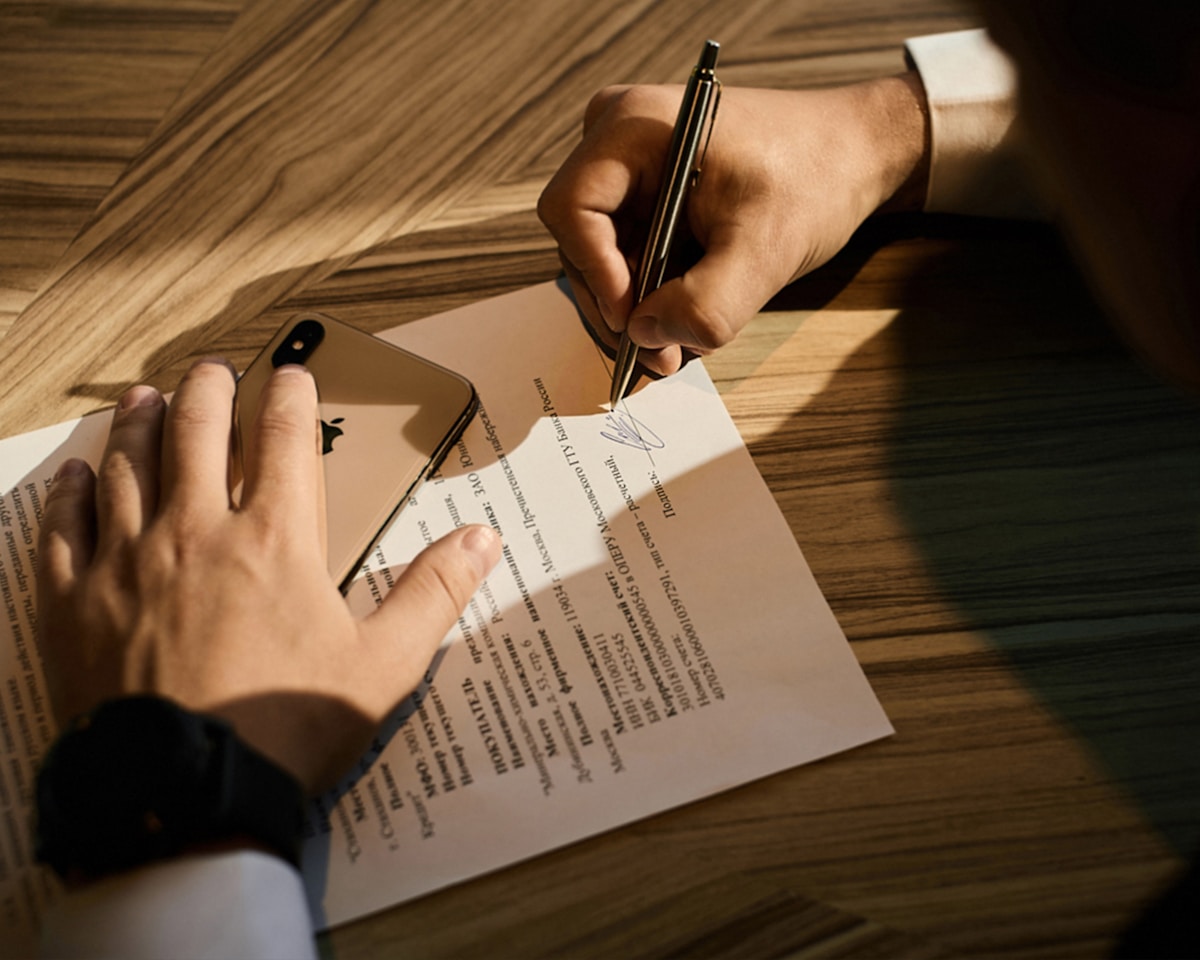 Mains signant un document sur un bureau en bois.