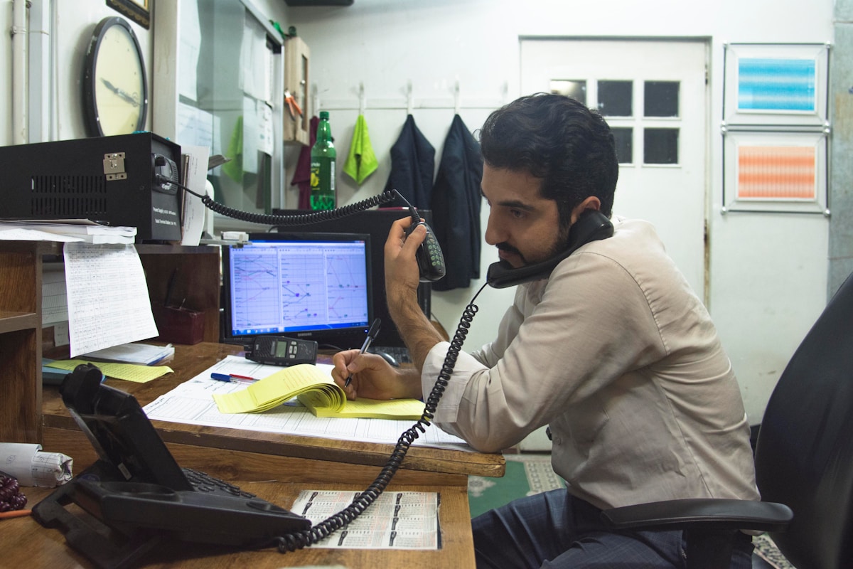 Homme au travail dans un bureau encombré, au téléphone et devant un ordinateur.
