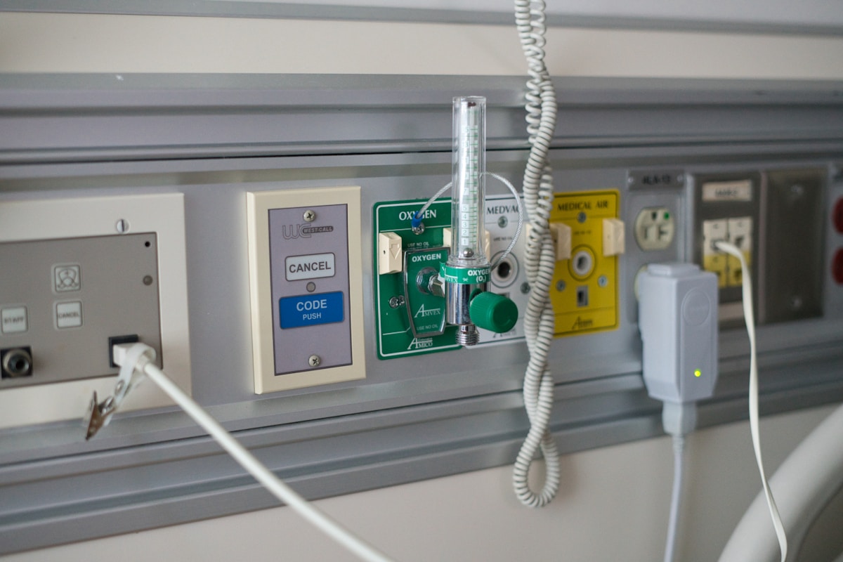 Équipement médical avec bouton d'urgence, régulateur d'oxygène et câbles électriques.