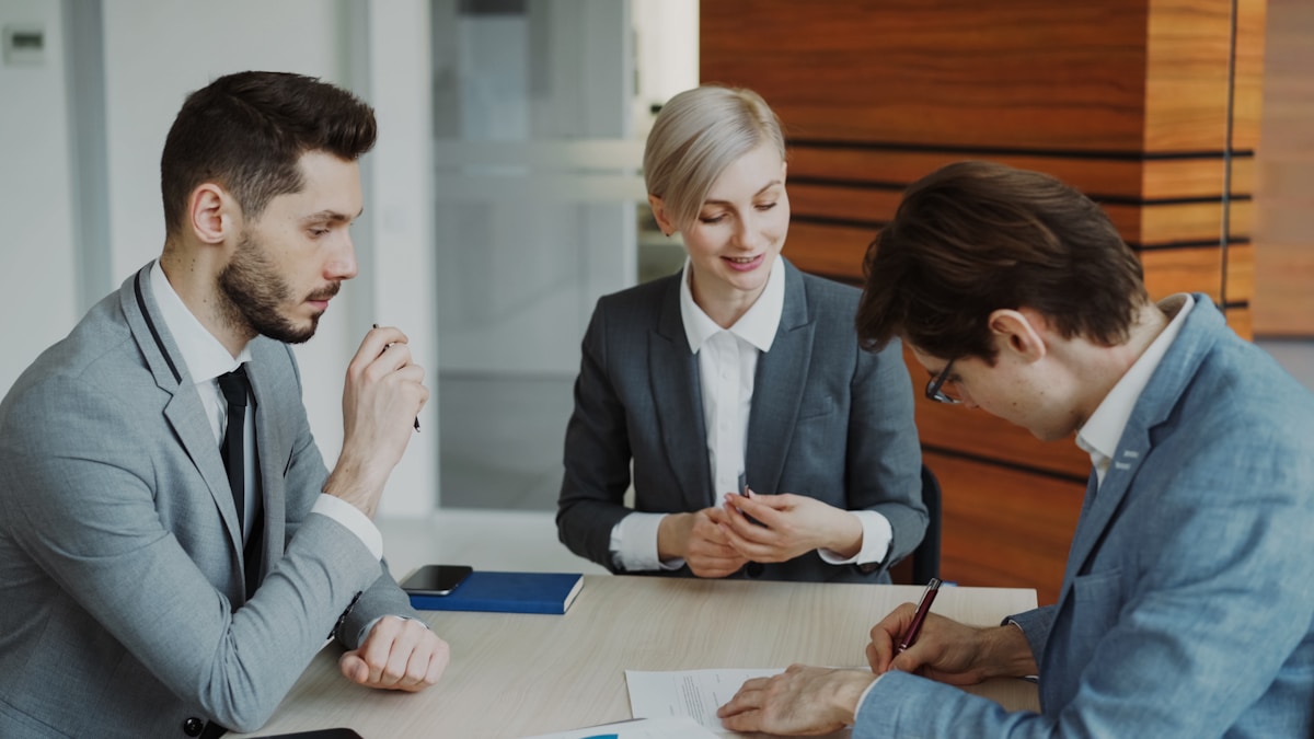 Trois professionnels en costume discutant autour d'une table de réunion.