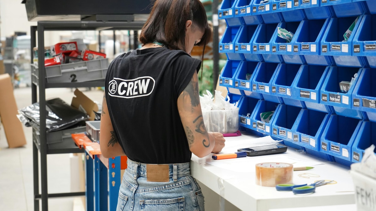 Employé en uniforme noir avec logo "CREW" au travail dans un entrepôt.