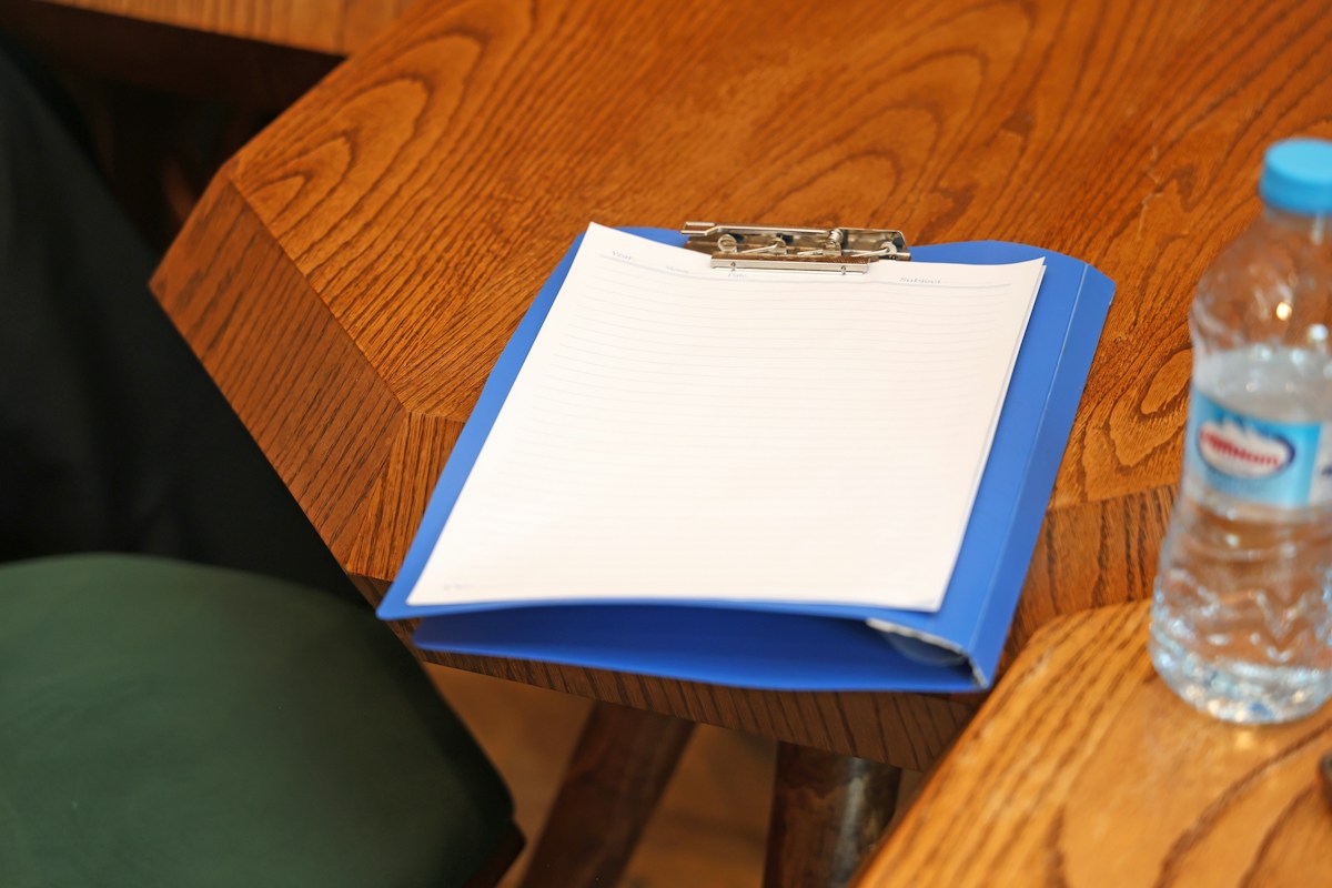 Presse-papiers bleu avec feuille blanche sur table en bois.