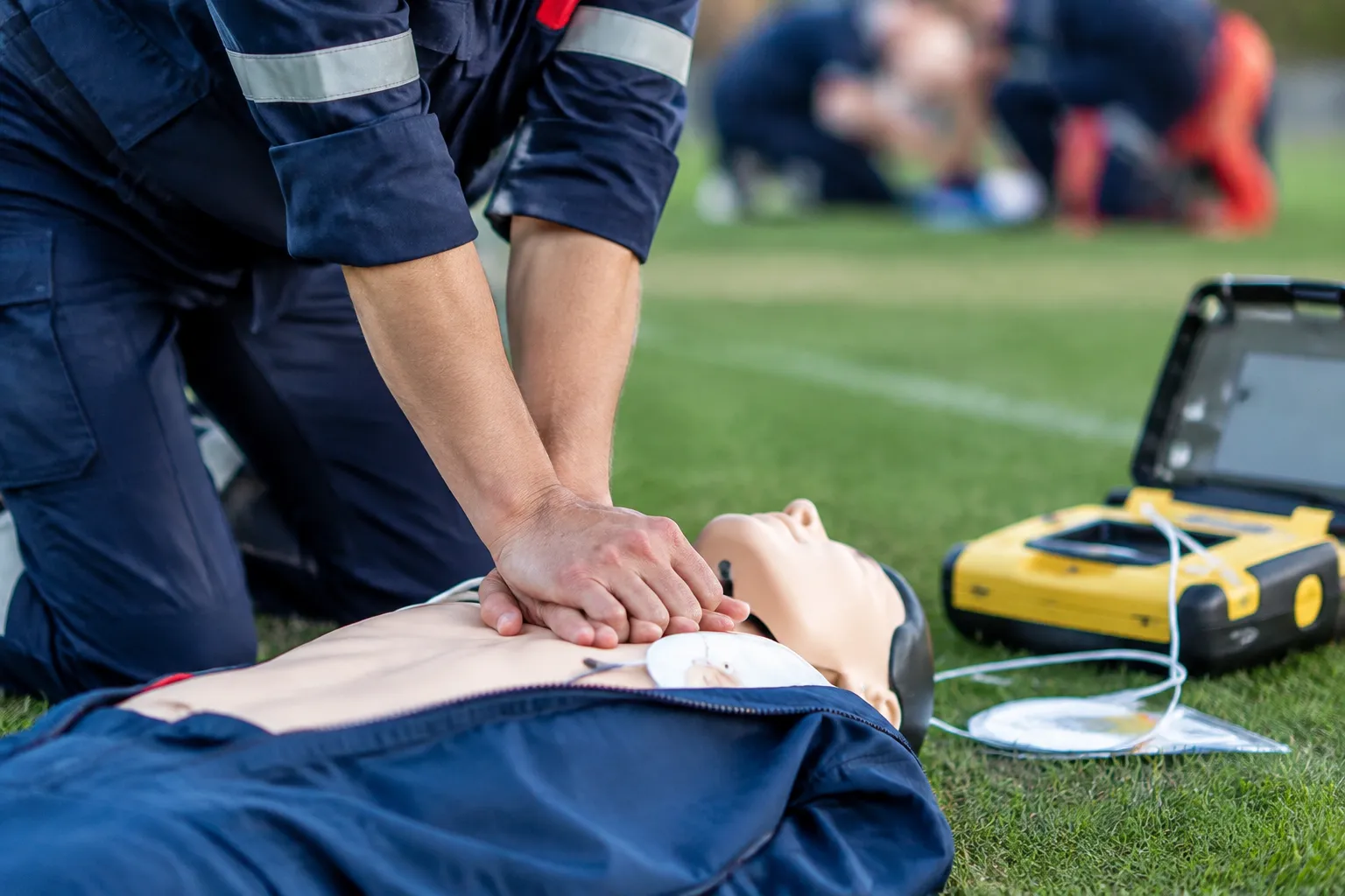 Secouriste pratiquant un massage cardiaque sur mannequin avec défibrillateur.